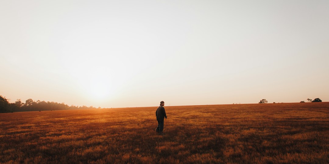 Person standing calmly in an open field at sunset, enjoying a peaceful moment