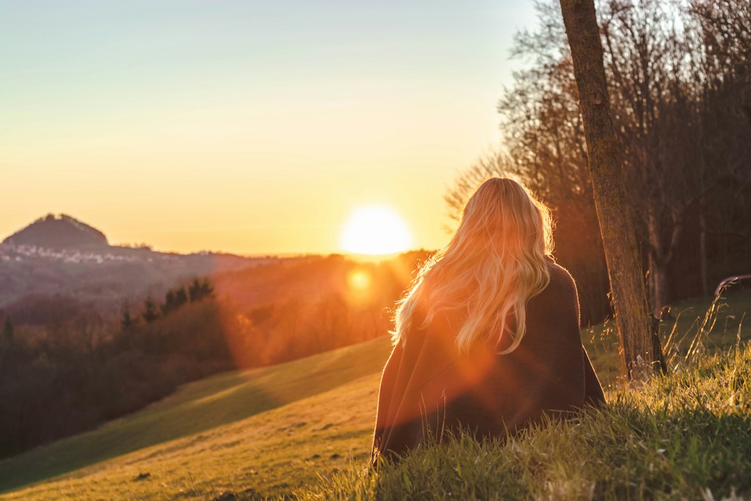 Woman sitting peacefully on the grass facing the sun, finding calm and freedom