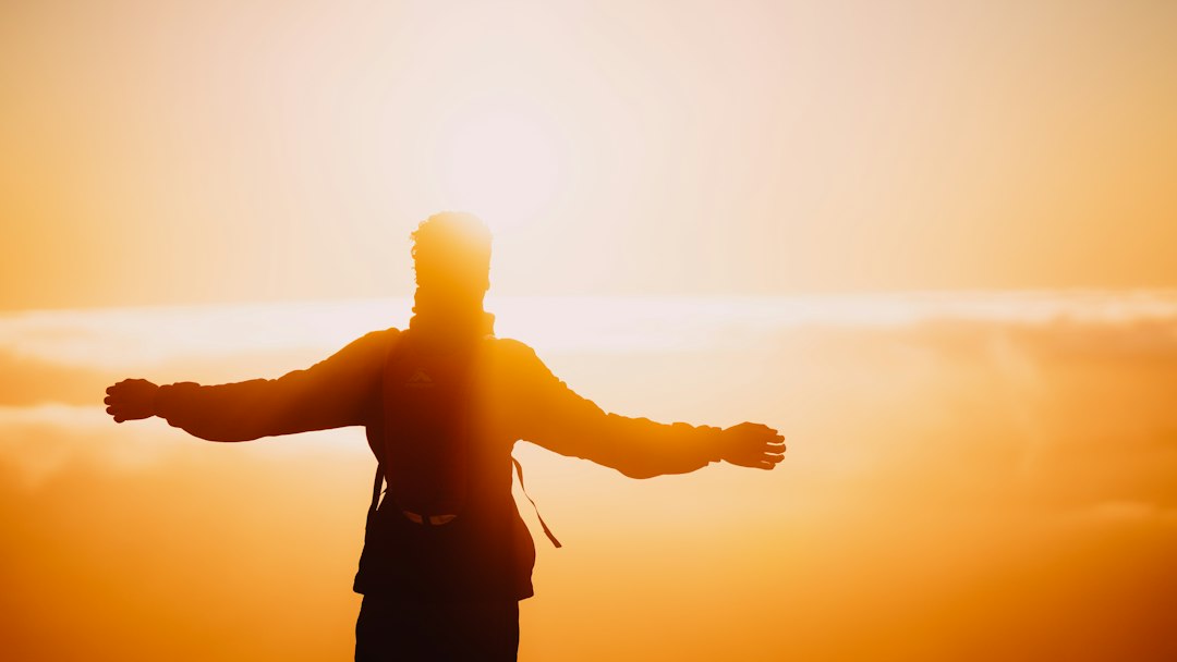 Person standing on a hilltop with arms outstretched, breathing in fresh open air