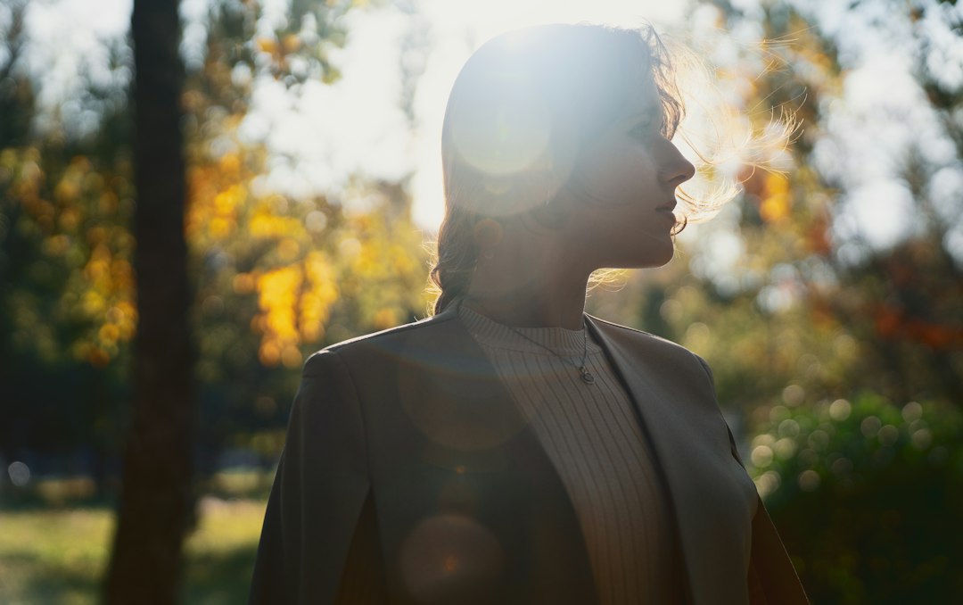 Woman in profile pausing in a sunlit autumn forest, bathed in warm golden light